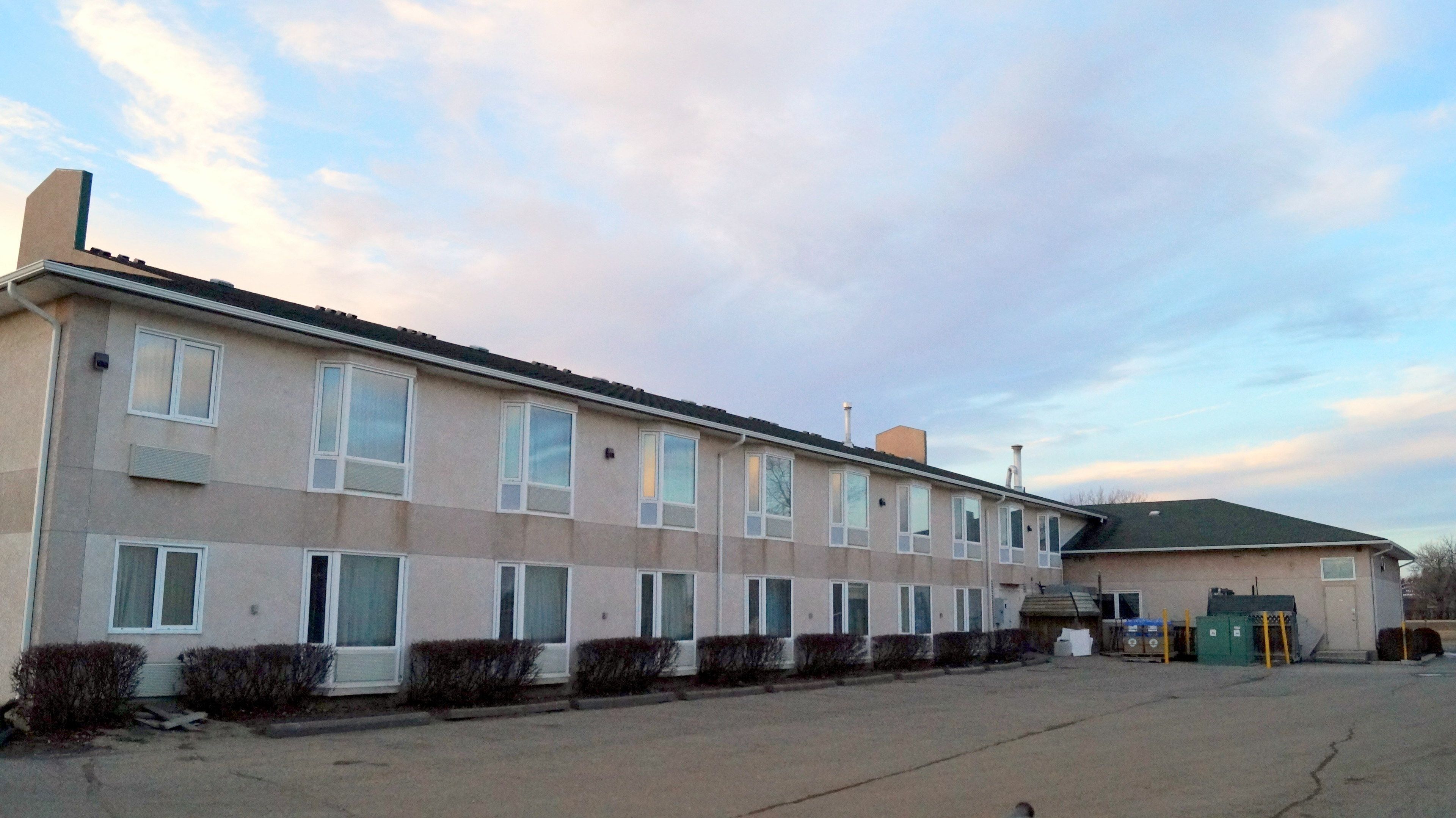 A multi-story building with a flat roof, large windows, and a parking lot in front.