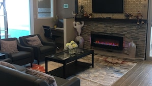 A modern living room with a fireplace, comfortable seating, and a flat-screen TV mounted on the wall. - Bay Hill Inns & Suites, Neepawa (Neepawa)