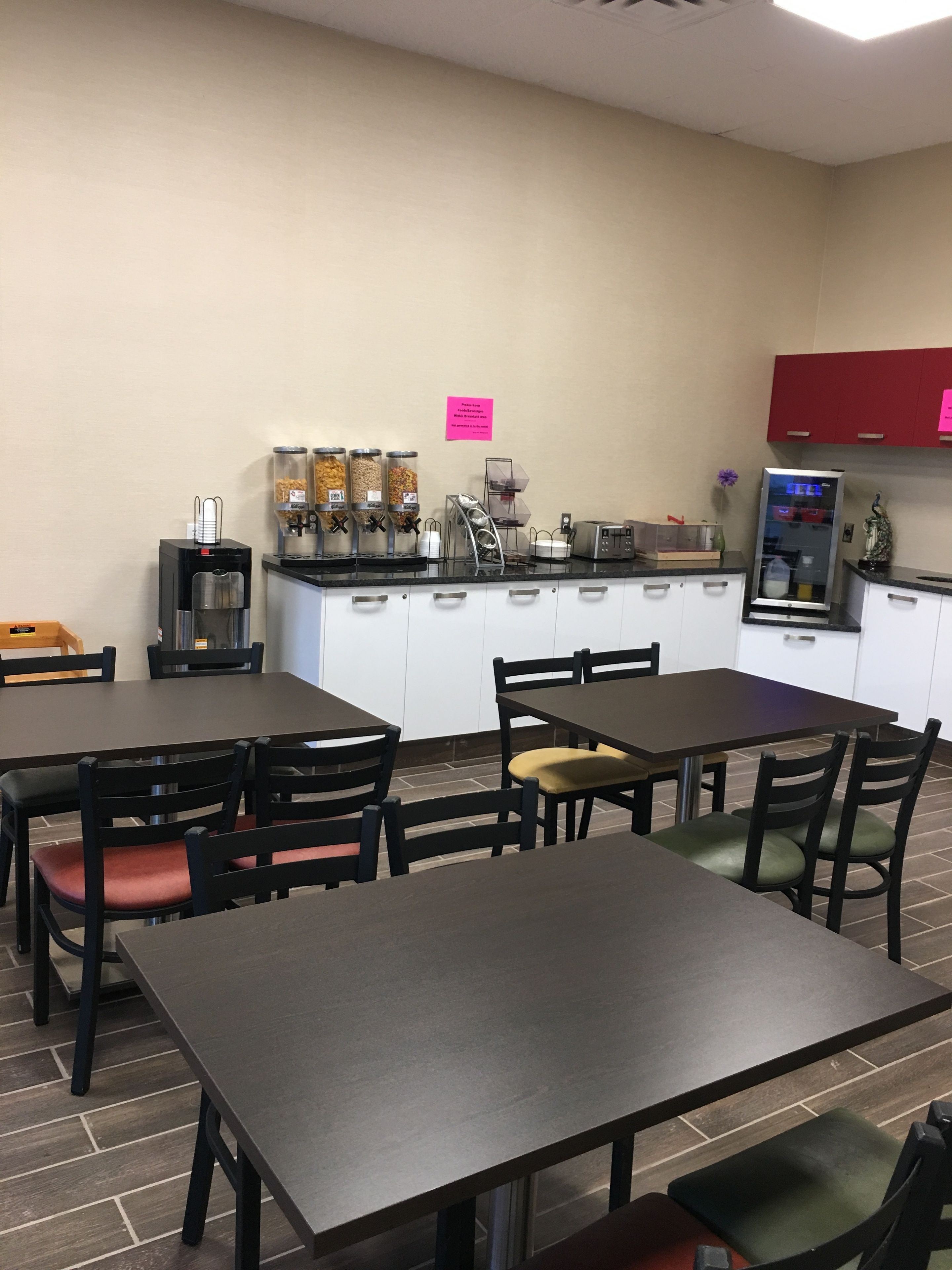 A dining area with tables and chairs, a coffee station with dispensers, and a refrigerator.