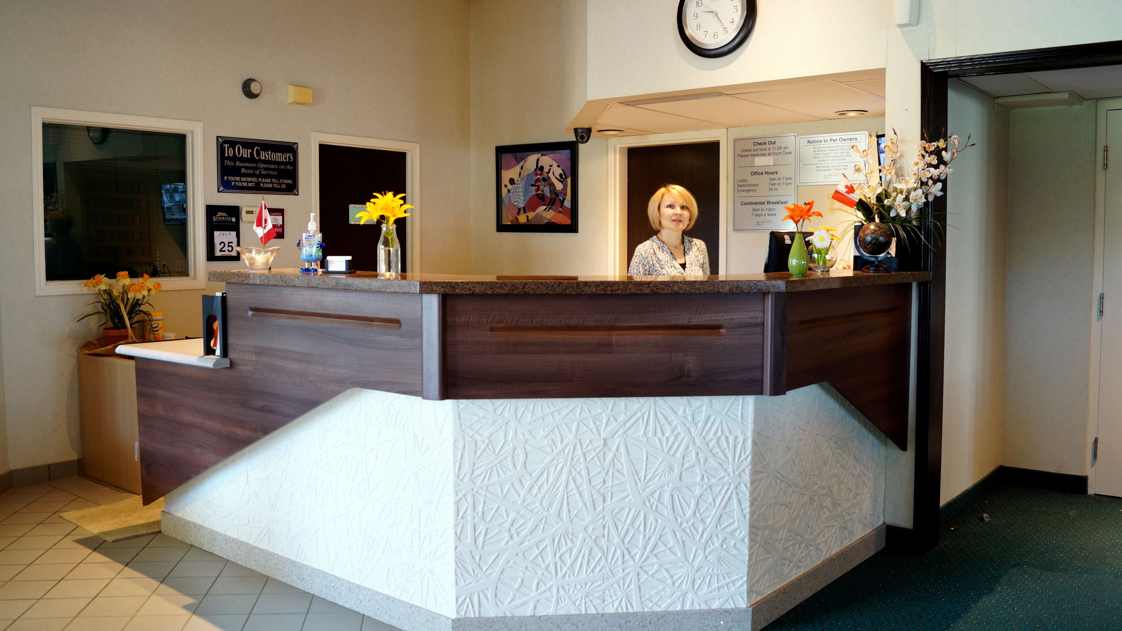 A reception desk with a clock, a sign for pet owners, and a flower vase.
