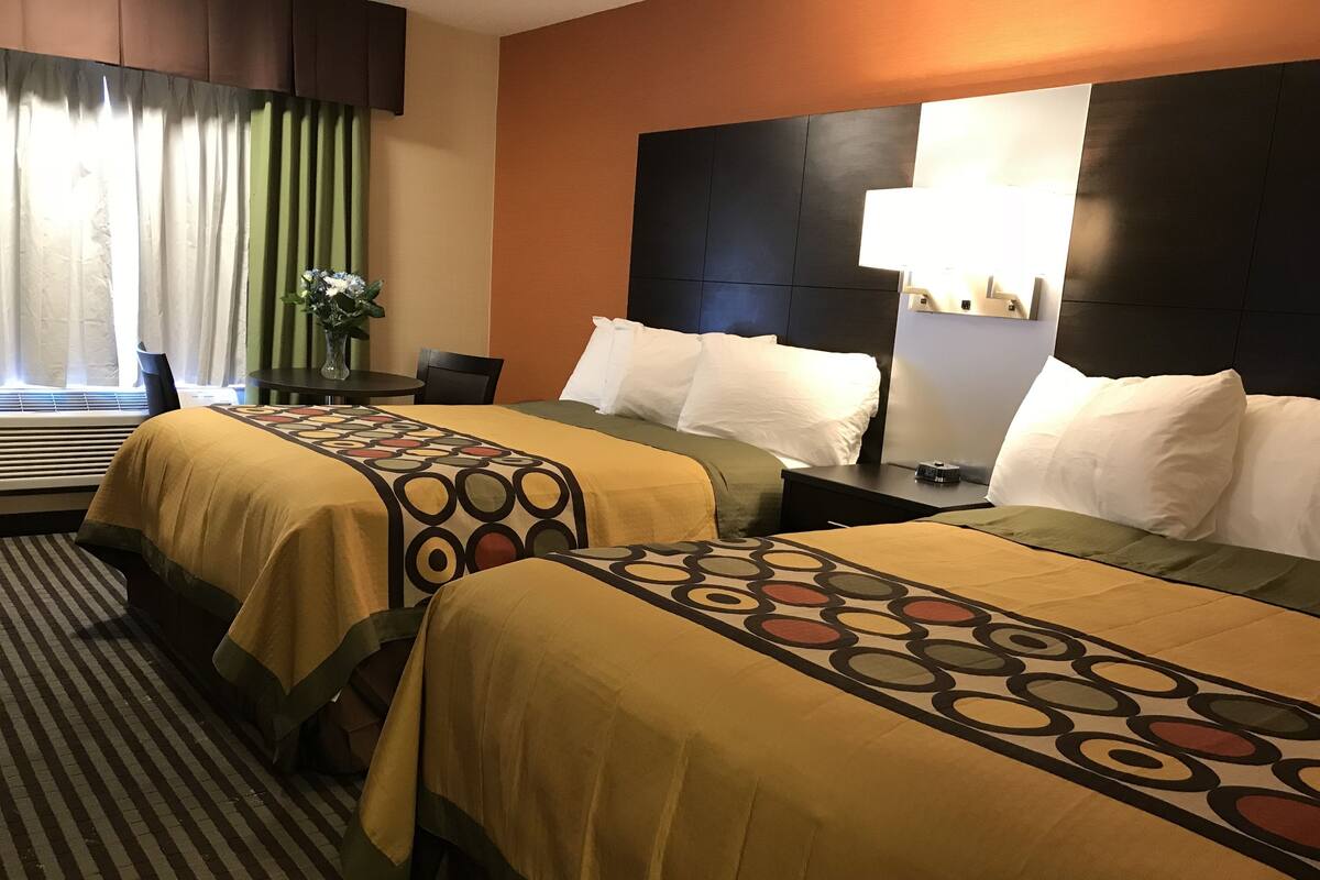 A hotel room with two beds, a desk, a chair, a lamp, and a window with curtains.