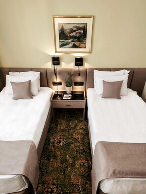 A hotel room with two beds, a nightstand with a plant, and a painting on the wall.