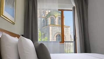 Une chambre d’hôtel avec un lit, un tableau accroché au mur et une vue sur un immeuble par la fenêtre.