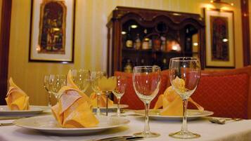 A dining table set with wine glasses and folded napkins, with a bar and framed pictures in the background.