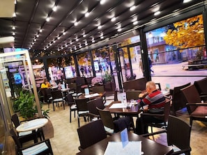 An indoor seating area with tables and chairs, a vending machine, and large windows with a view of the street outside.