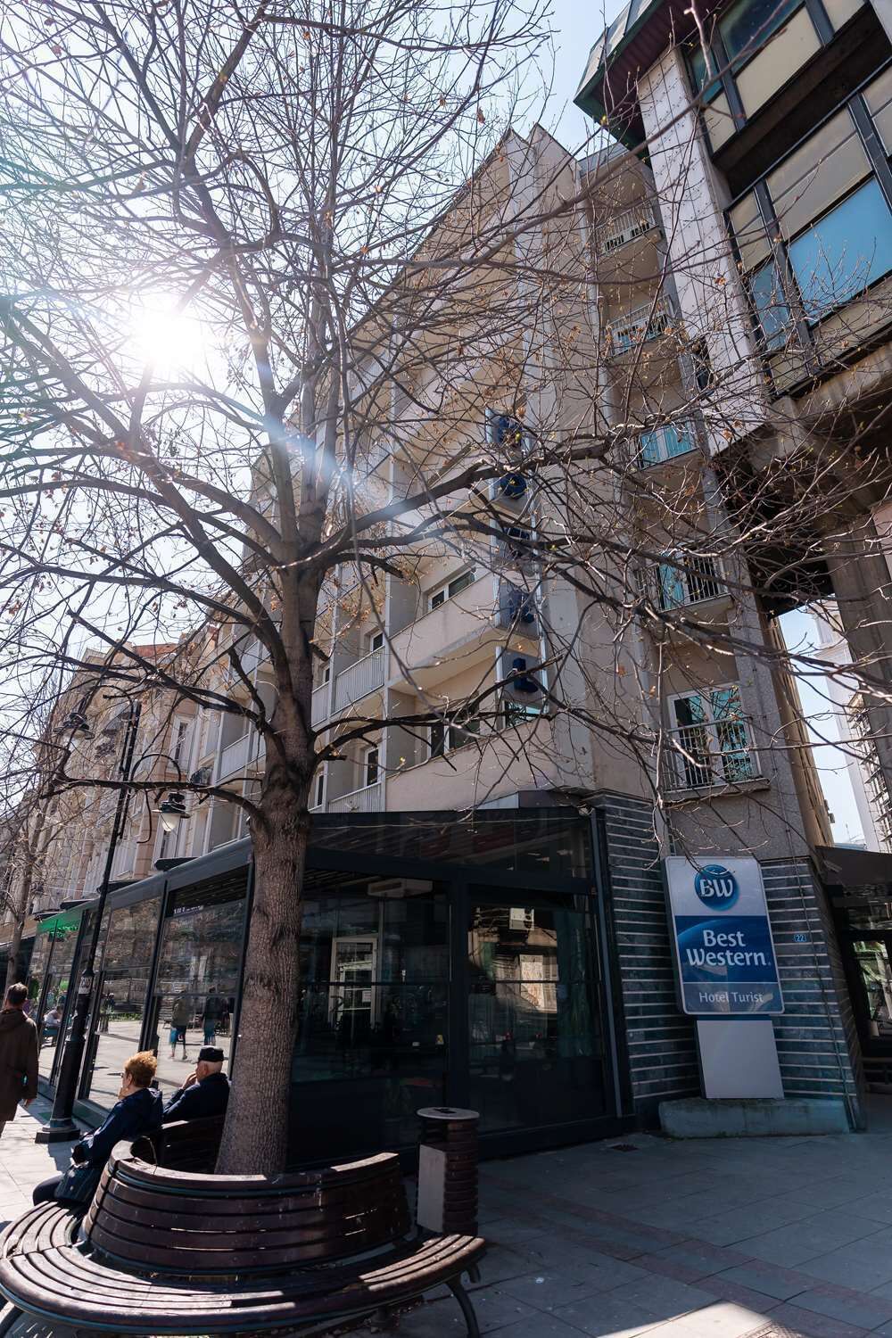Un bâtiment portant l’enseigne d’un hôtel Best Western, avec un arbre devant et un banc.