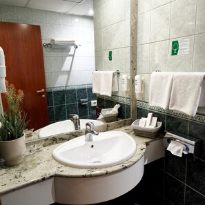 Un baño con lavamanos, espejo, toallero y zona de ducha.
