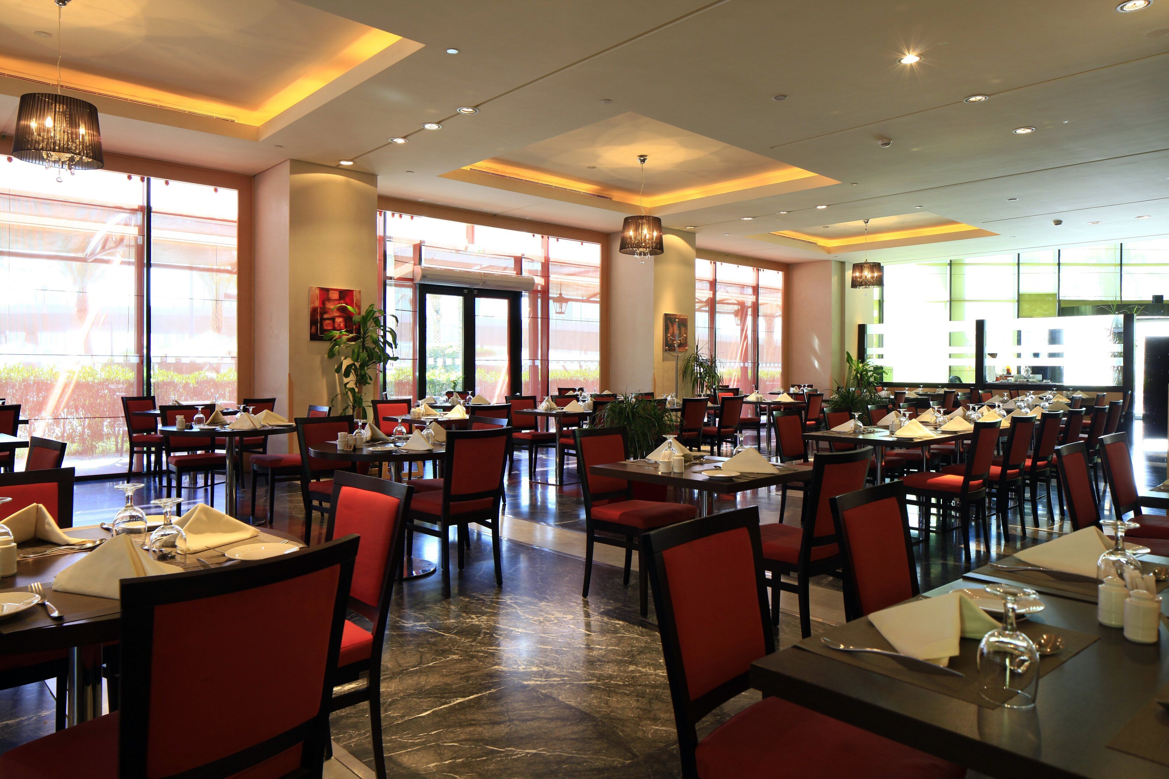 A spacious dining area with multiple tables and chairs, large windows, and ceiling lights.