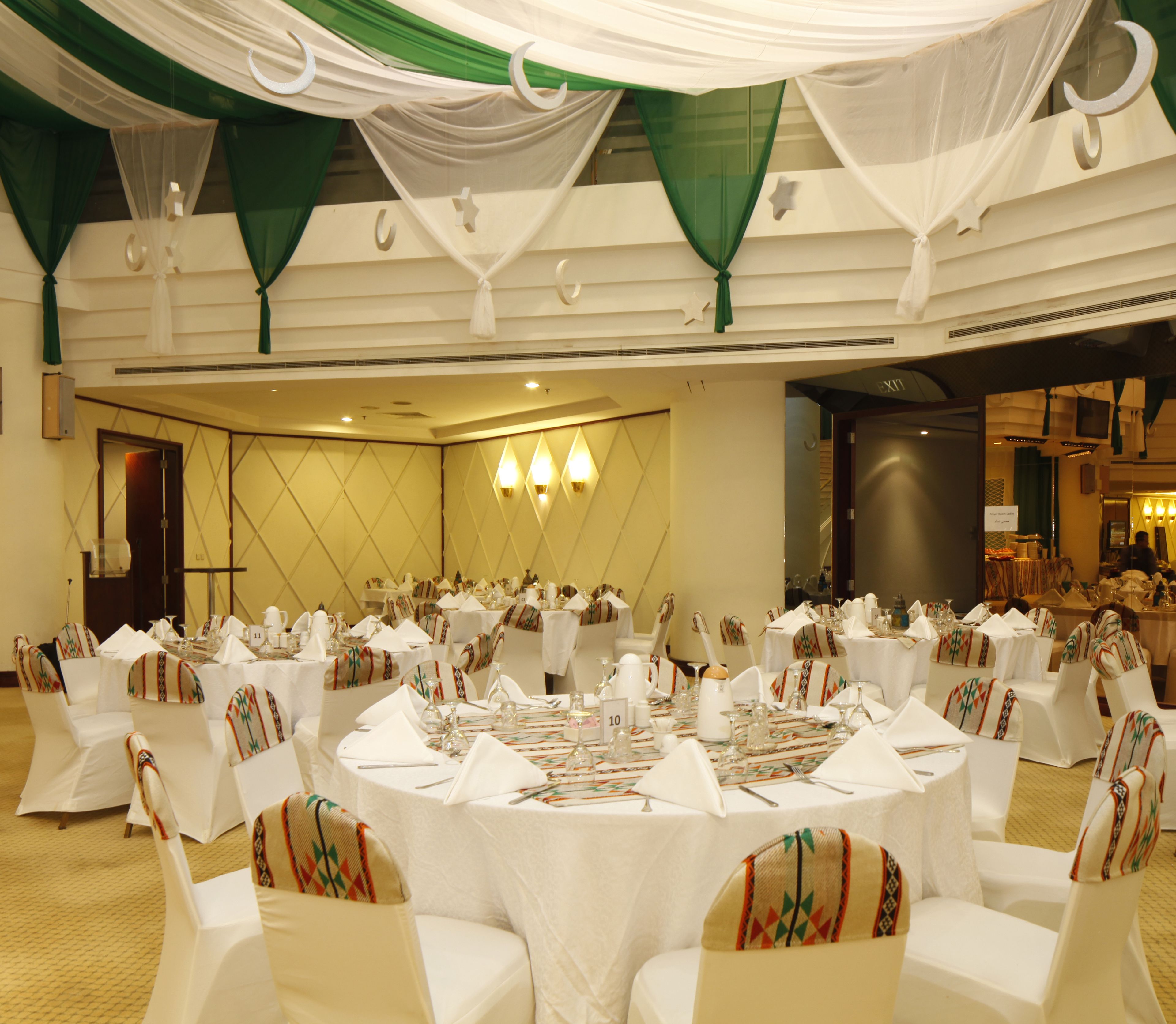 A banquet hall with round tables set for a formal event, featuring white tablecloths and chairs with patterned covers.