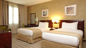 A hotel room with two beds, a desk, a chair, and artwork on the walls.
