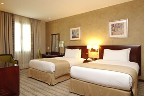 A hotel room with two beds, a desk, a chair, and artwork on the walls.