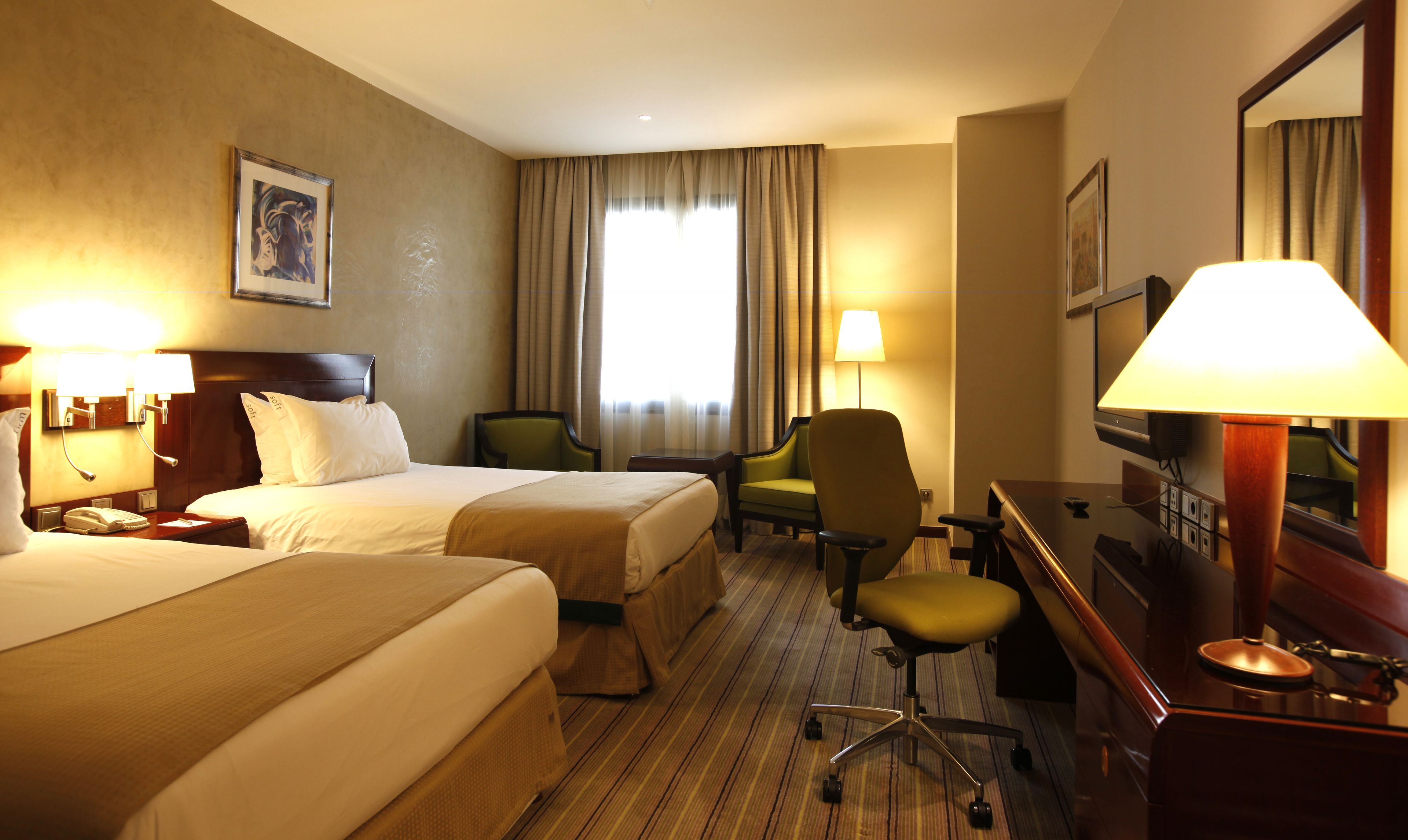 A hotel room with two beds, a desk, a chair, a TV, and a lamp.