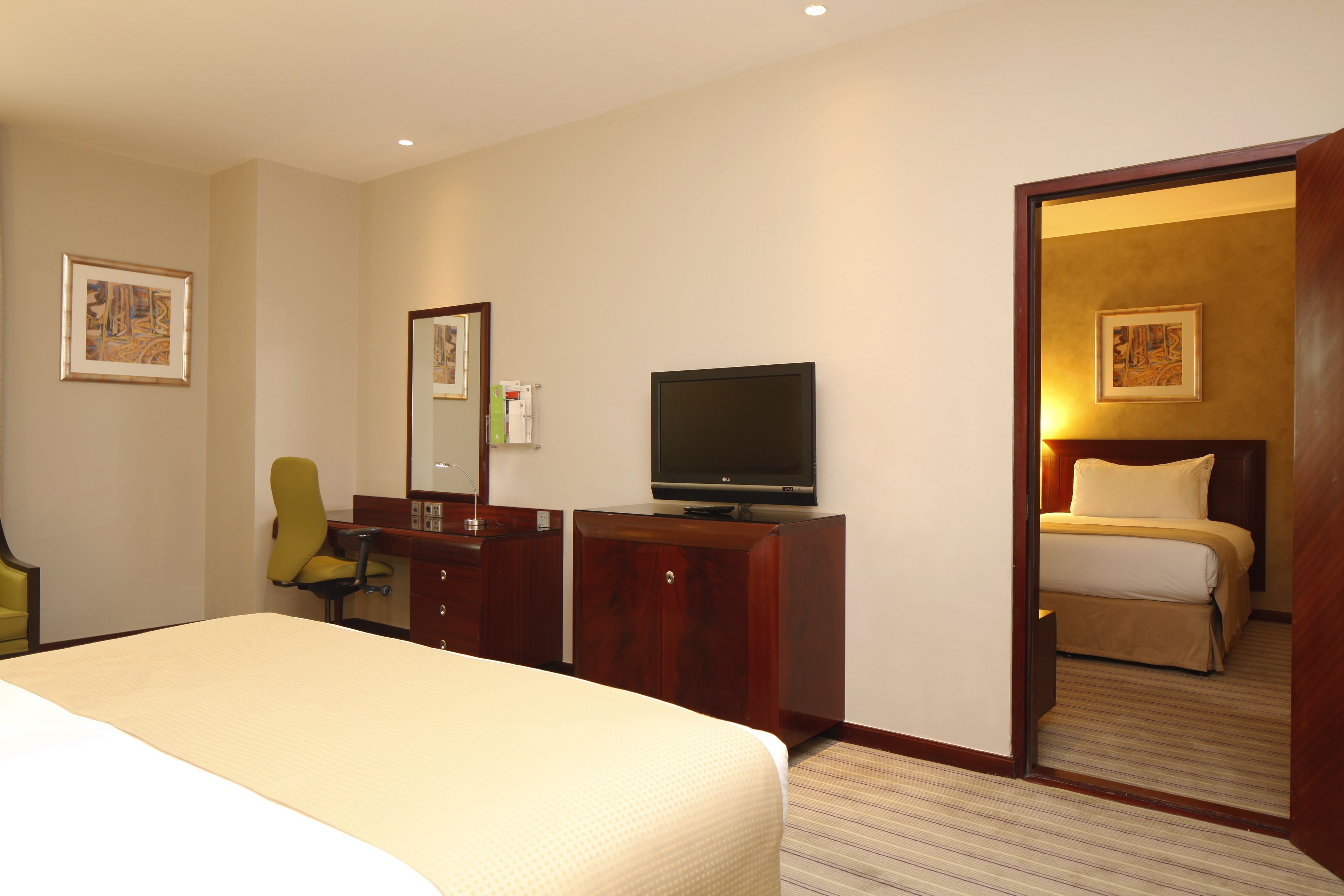 Une chambre d’hôtel avec un lit, un téléviseur posé sur une commode en bois, un bureau avec une chaise et une porte donnant sur une autre pièce.