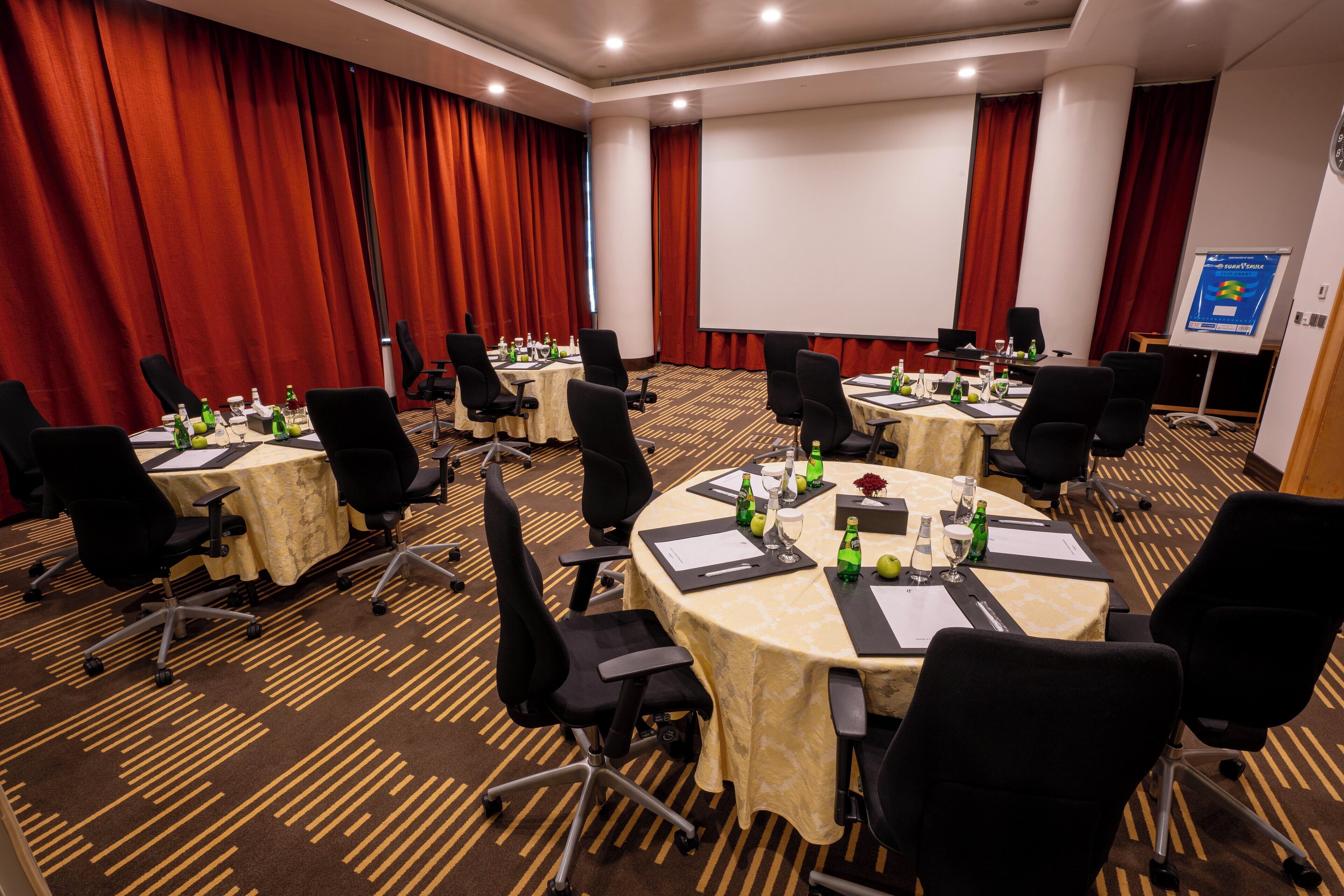 Un salón de conferencias con varias mesas, sillas y una pantalla de proyección.