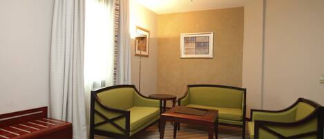 A hotel room with two green armchairs, a small wooden table, and a red sofa.