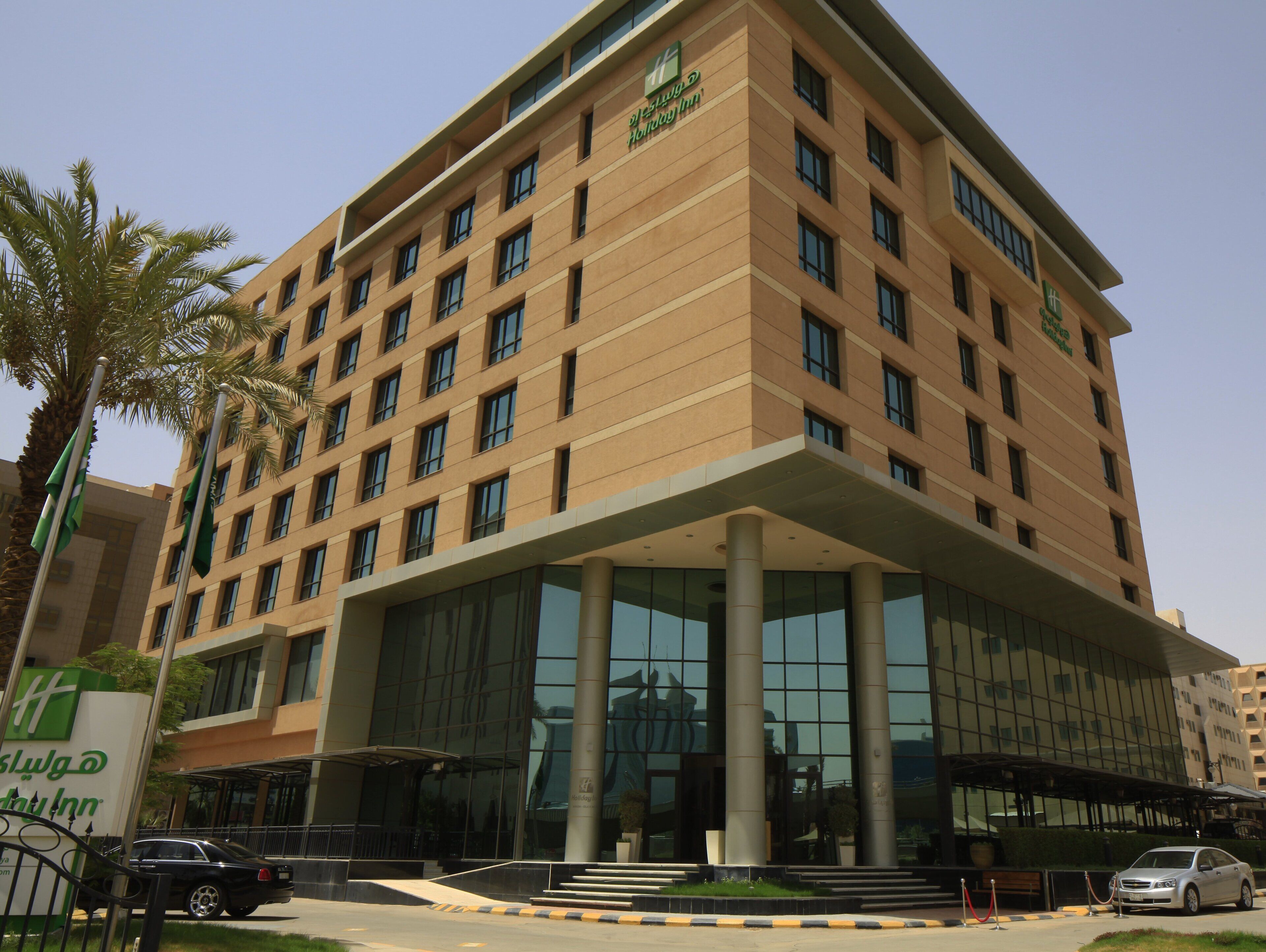 A multi-story hotel with a modern design, featuring a large glass entrance and a prominent outdoor seating area.