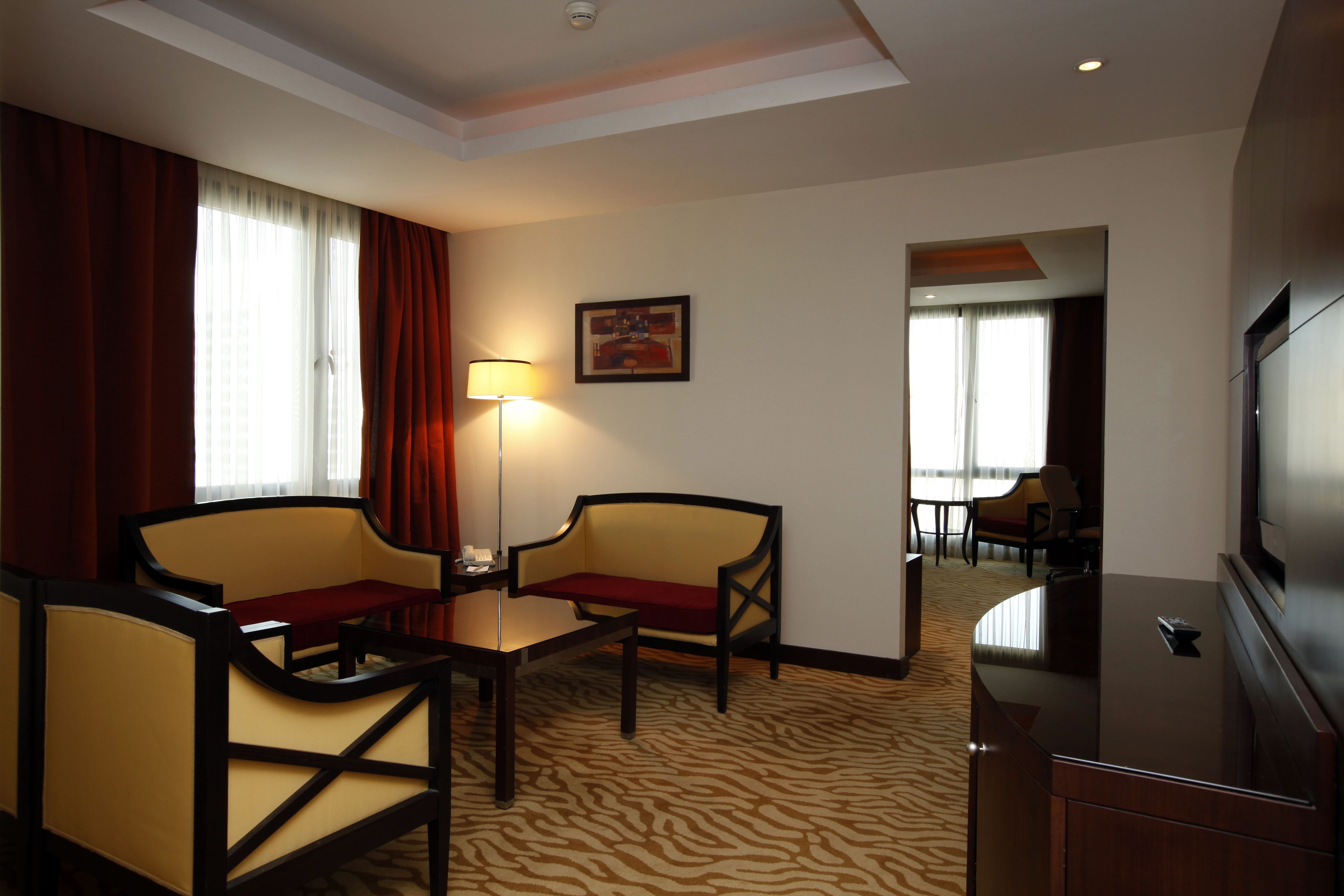A hotel room with a zebra-patterned carpet, two armchairs, a small table, a lamp, a television, and a painting on the wall.