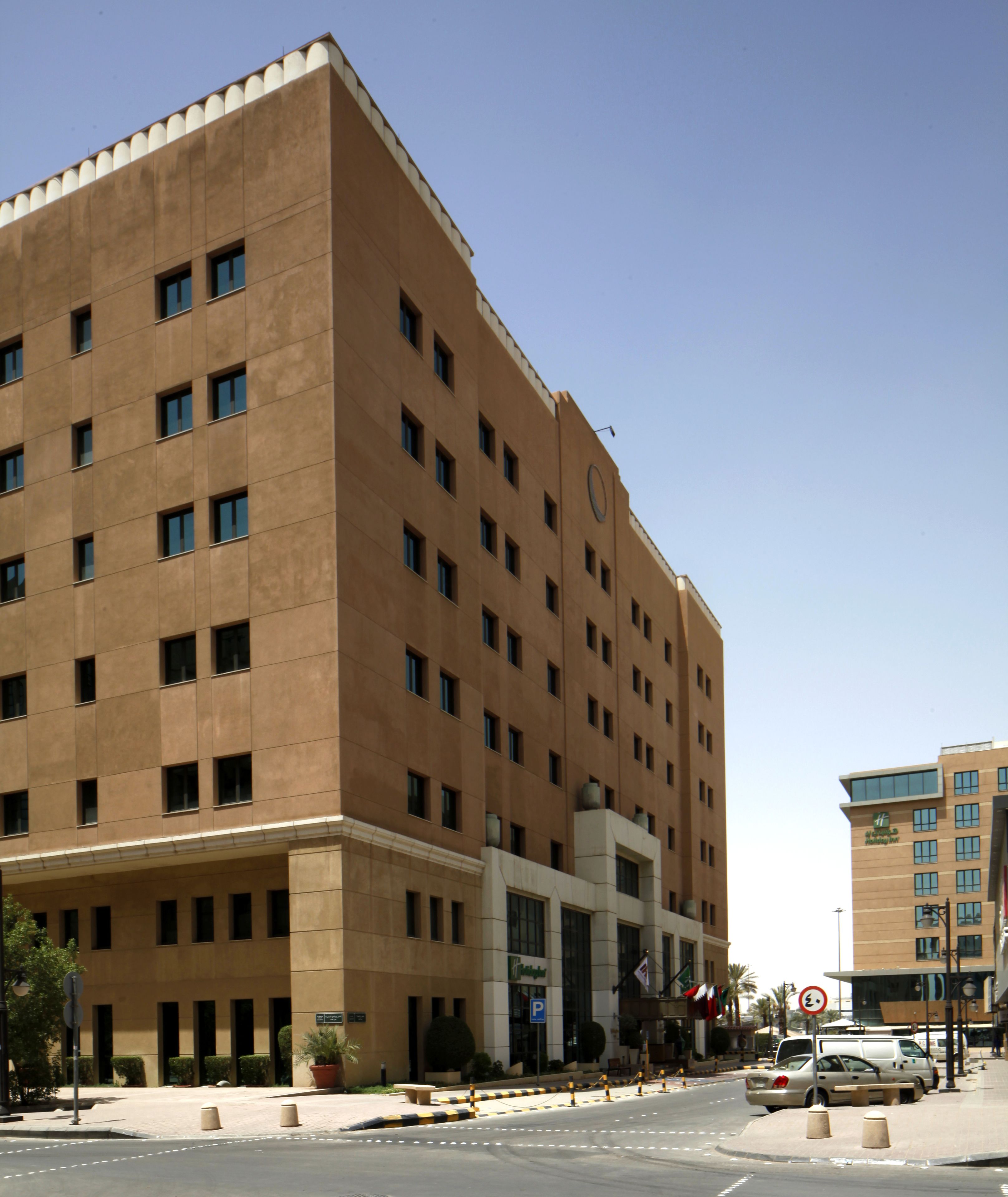 A large, multi-story hotel with a modern architectural design, featuring a prominent entrance and a parking area in front.
