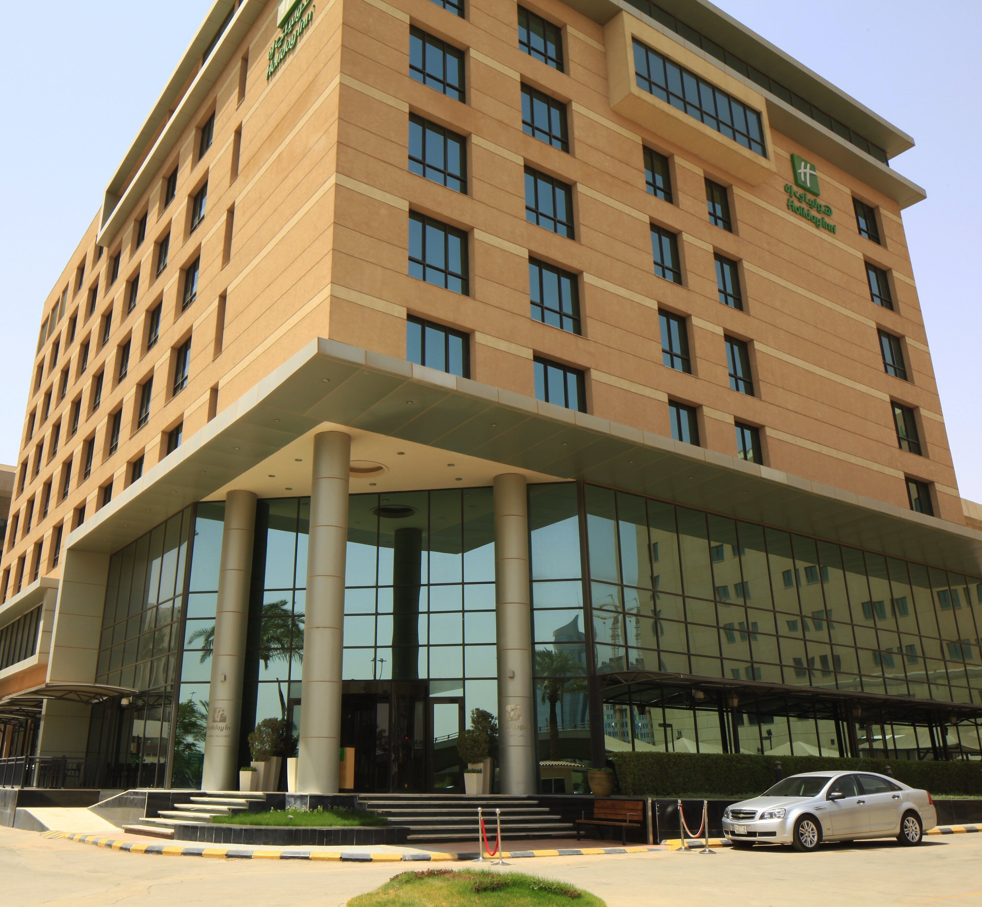 A multi-story hotel with a modern design, featuring a prominent entrance with glass doors and a covered walkway.