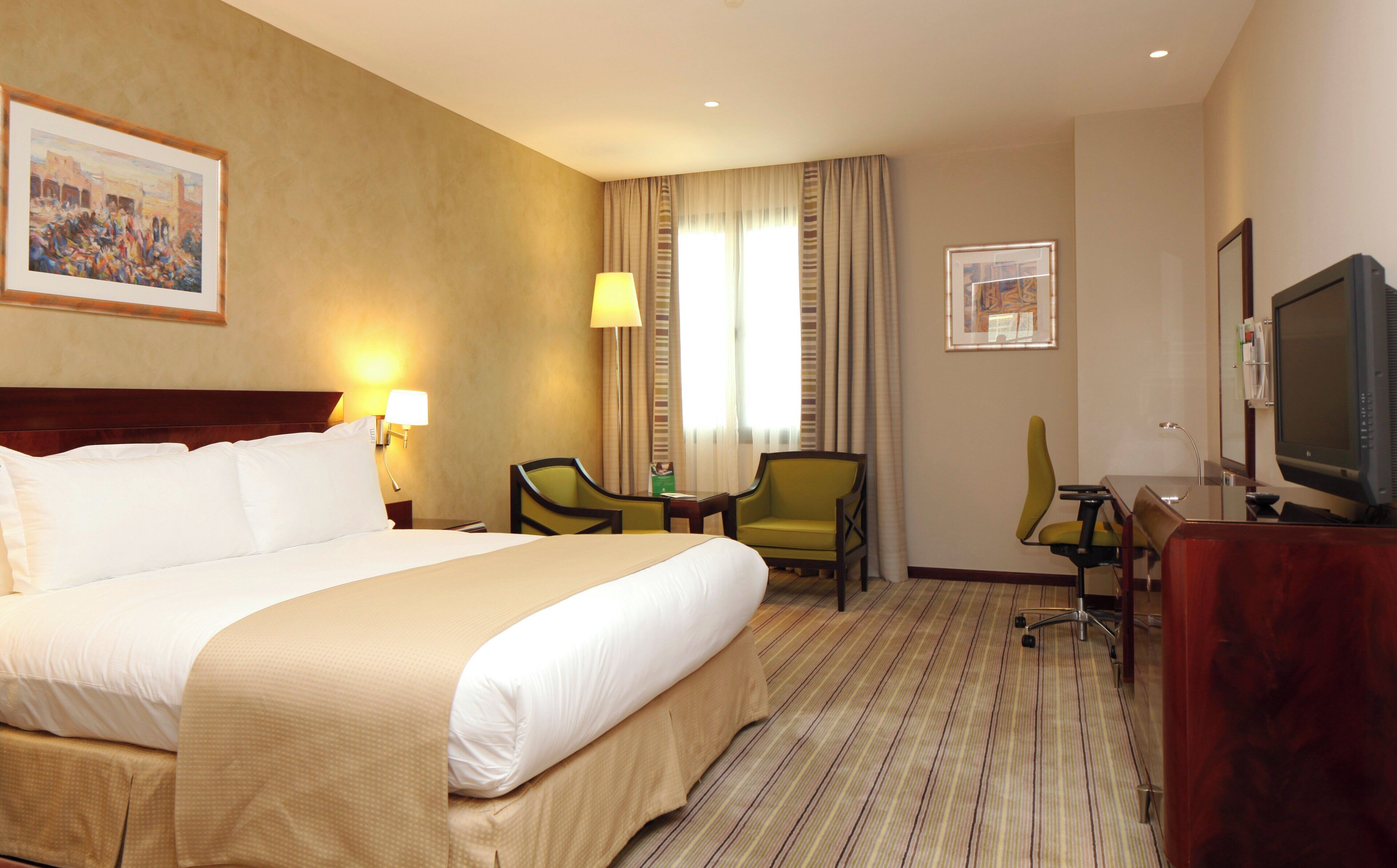 A hotel room with a large bed, a desk with a chair, a television, and artwork on the walls.