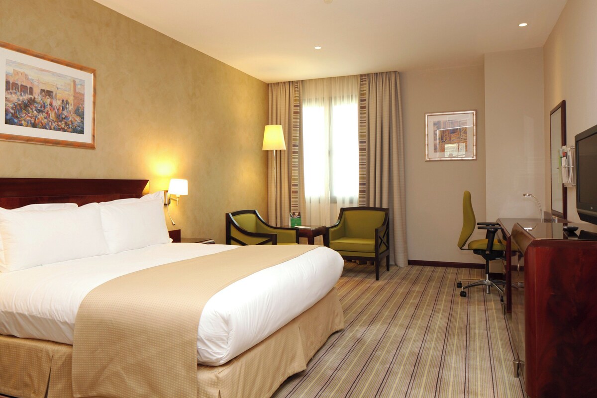 A hotel room with a large bed, a desk with a chair, a television, and two lamps.