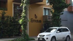 Un SUV blanco estacionado frente a un edificio con un muro amarillo y un logotipo que dice "Emaus".