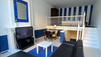 Una sala de estar con un sofá negro, una mesa de centro blanca, un televisor y una araña.