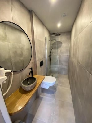 Un baño moderno con ducha envuelta en vidrio, tocador de madera con lavabo y un inodoro.