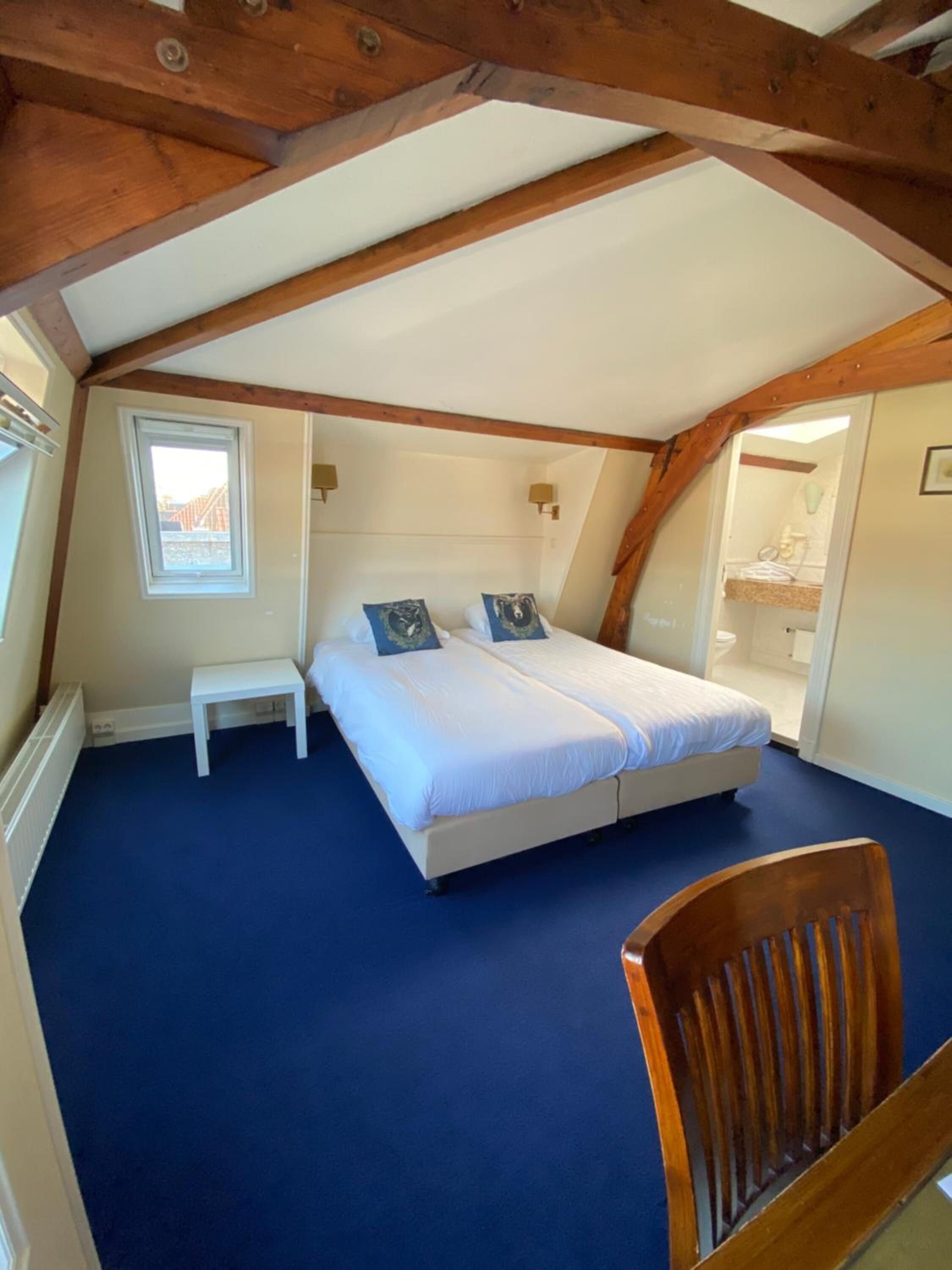 Un dormitorio con una cama grande, una mesita, una silla y un ventanal.