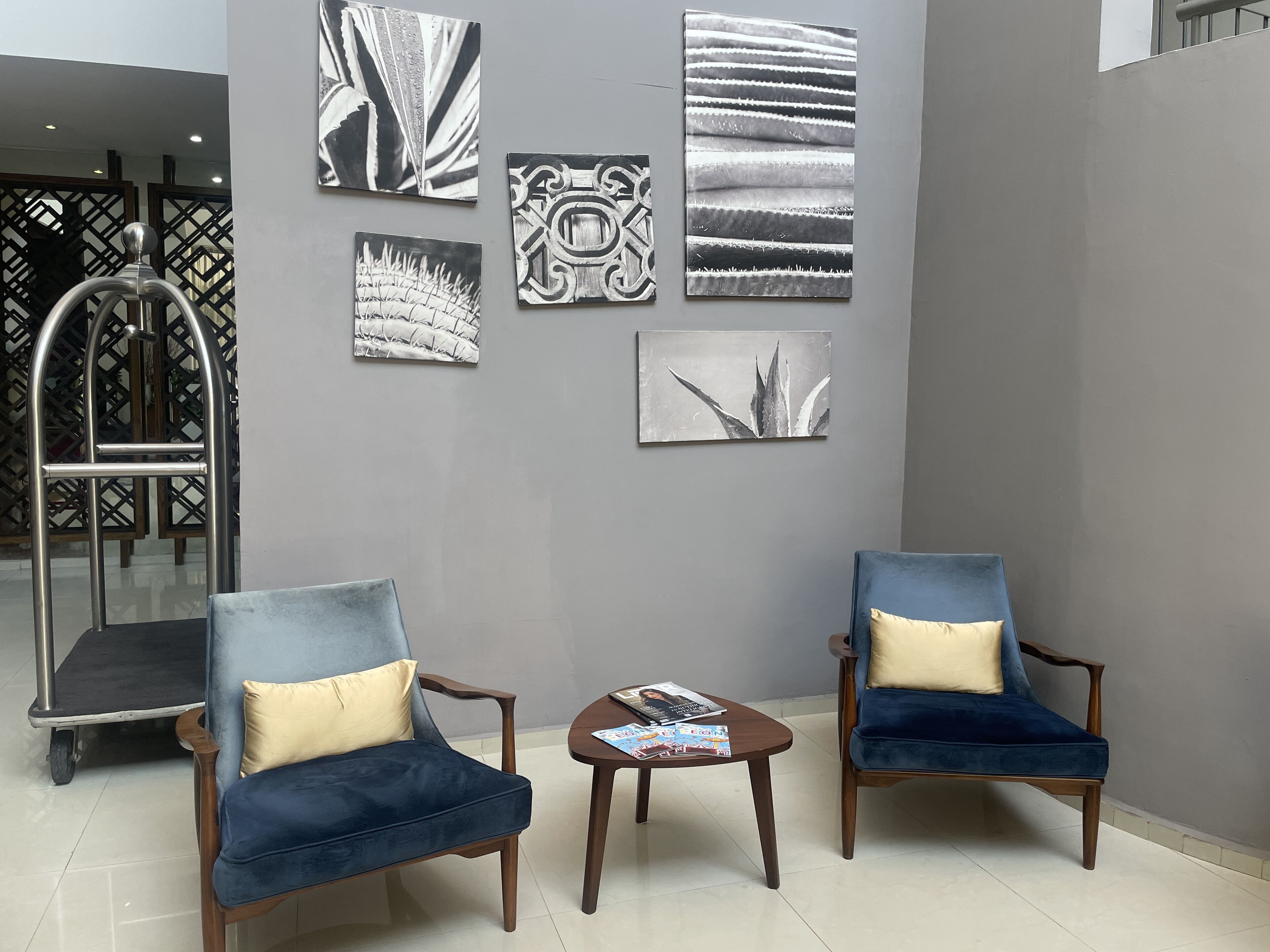 A lobby with two blue armchairs, a small table with magazines, and four artworks on the wall.