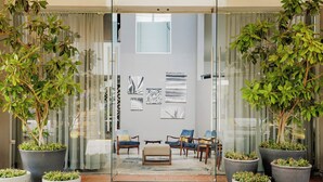 Een moderne lobby met glazen deuren, potplanten en een zithoek met stoelen en een bank.