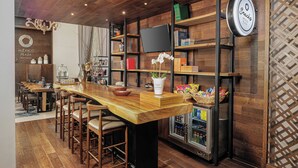 Een bar met houten barstoelen, een lange houten toonbank, een aan de muur bevestigde televisie en planken vol met snacks en drankjes.