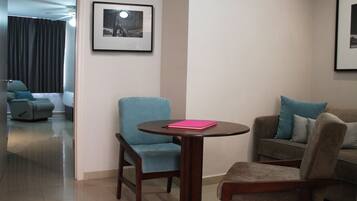 Una sala de estar moderna con una mesa redonda de madera, dos sillones y un sofá. Se observa un cuadro en la pared y un ventilador de techo.