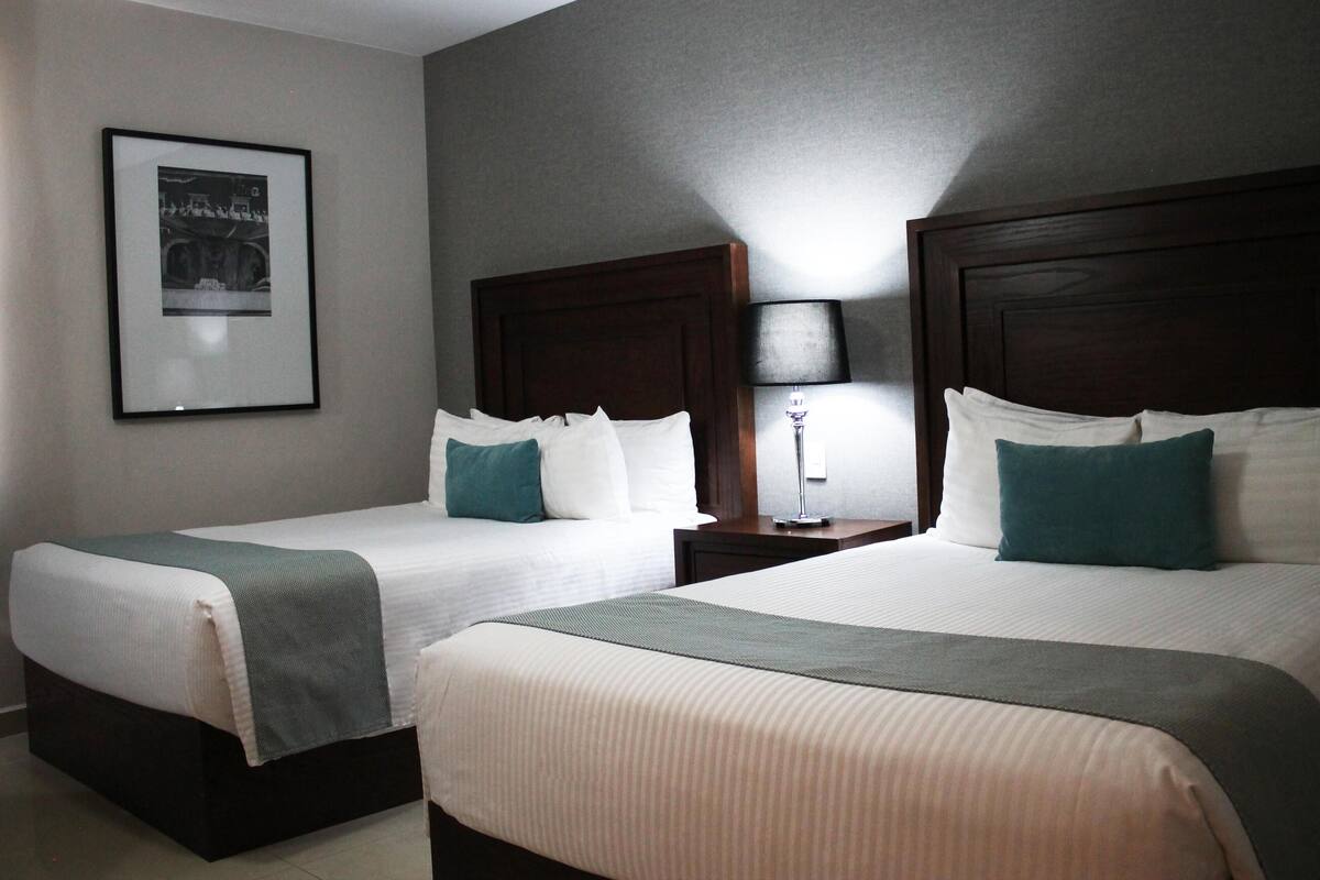 A hotel room with two beds, a framed picture on the wall, and a nightstand with a lamp.