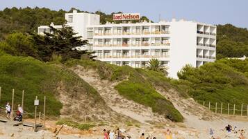 A hotel with multiple balconies and a beach in the foreground.