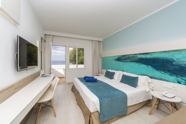 Habitación de hotel moderna con una cama grande, un escritorio, televisión y vistas al mar a través de la ventana.