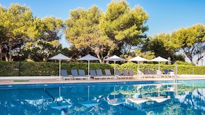 Piscina con sillas de descanso y sombrillas, rodeada de árboles.