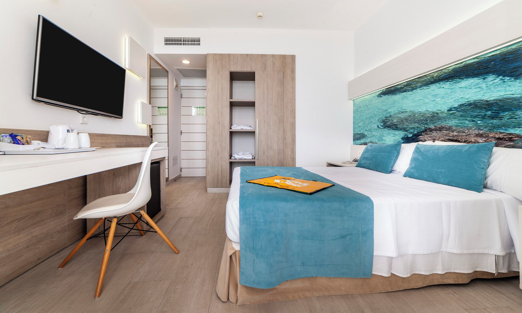 A hotel room with a bed, a desk, a chair, a TV, and a large window with a view of water.