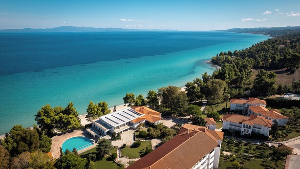 An aerial view of a coastal property with a swimming pool, terraced houses, and a clear view of the sea. - Canvas by Mitsis Alexander the Great (Kassandra)