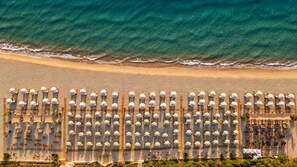 Vista aérea de una playa con hileras de sombrillas y sillas de descanso, lo que sugiere un entorno de resort.