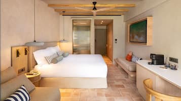 A modern hotel room with a large bed, a seating area with a coffee machine, and a painting on the wall.