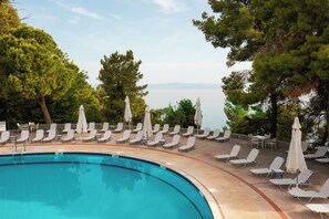 Una piscina al aire libre, sombrillas, sillones reclinables de piscina