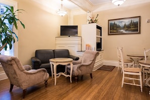 A living room with a fireplace, a television, a painting, and a dining area with chairs and a table. - Grant Hotel (San Francisco)