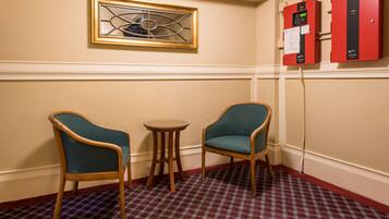 A room with two chairs, a small table, a patterned carpet, a framed artwork, and red filing cabinets.