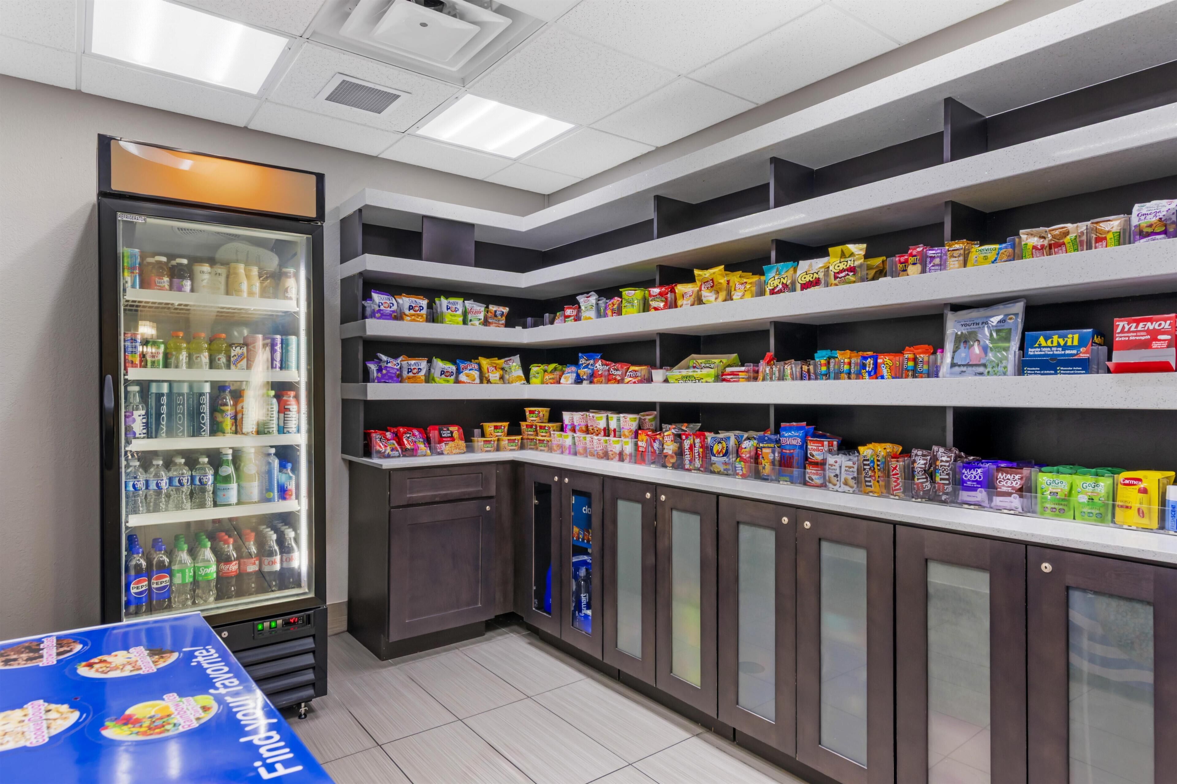 Espaço com lanches e bebidas, prateleiras repletas de produtos diversos e um refrigerador.
