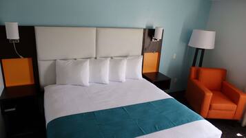 A hotel room with a large bed, two bedside tables, an orange armchair, and a nightstand with a lamp.