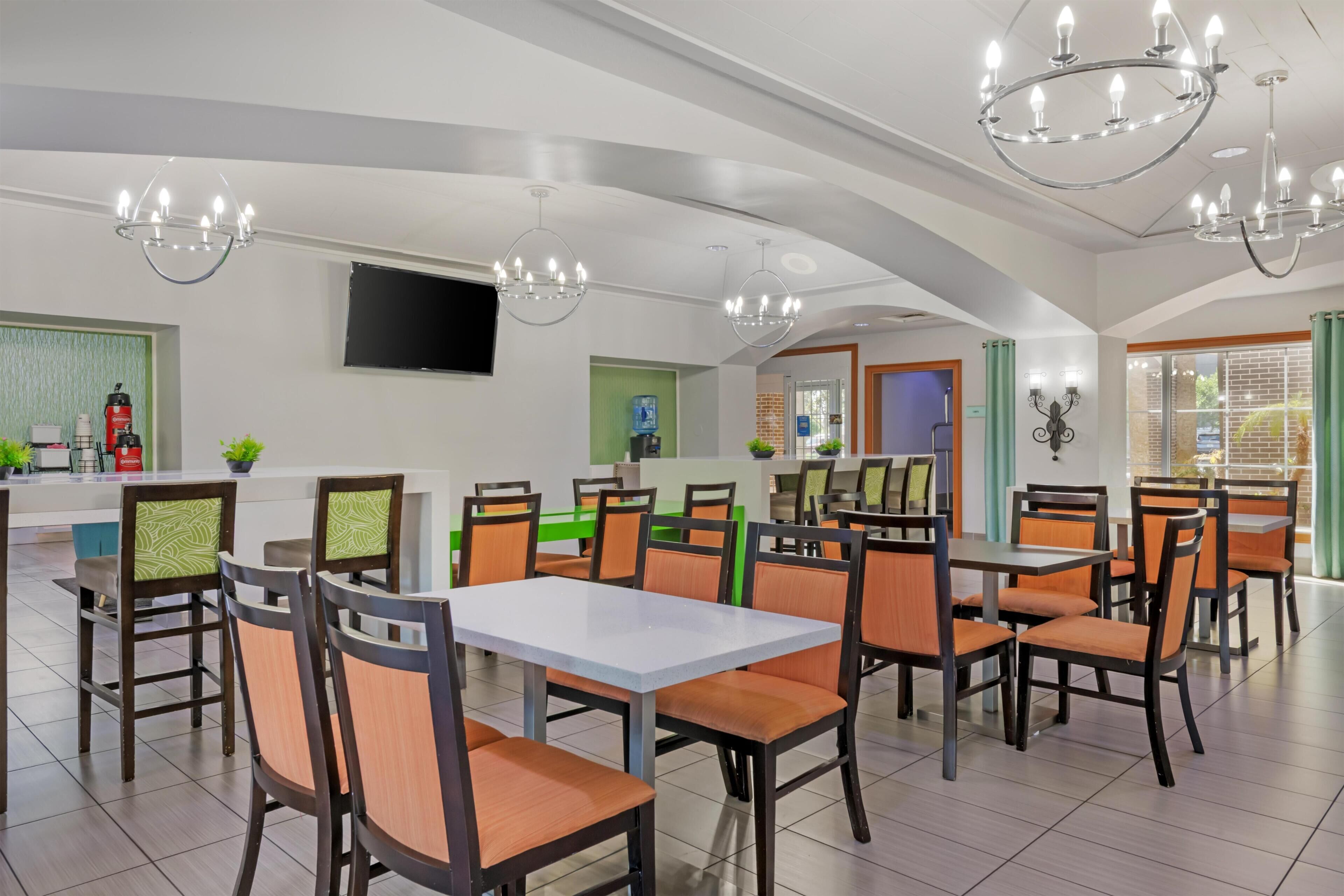 A modern dining area with tables and chairs, a kitchen counter, and a television mounted on the wall.