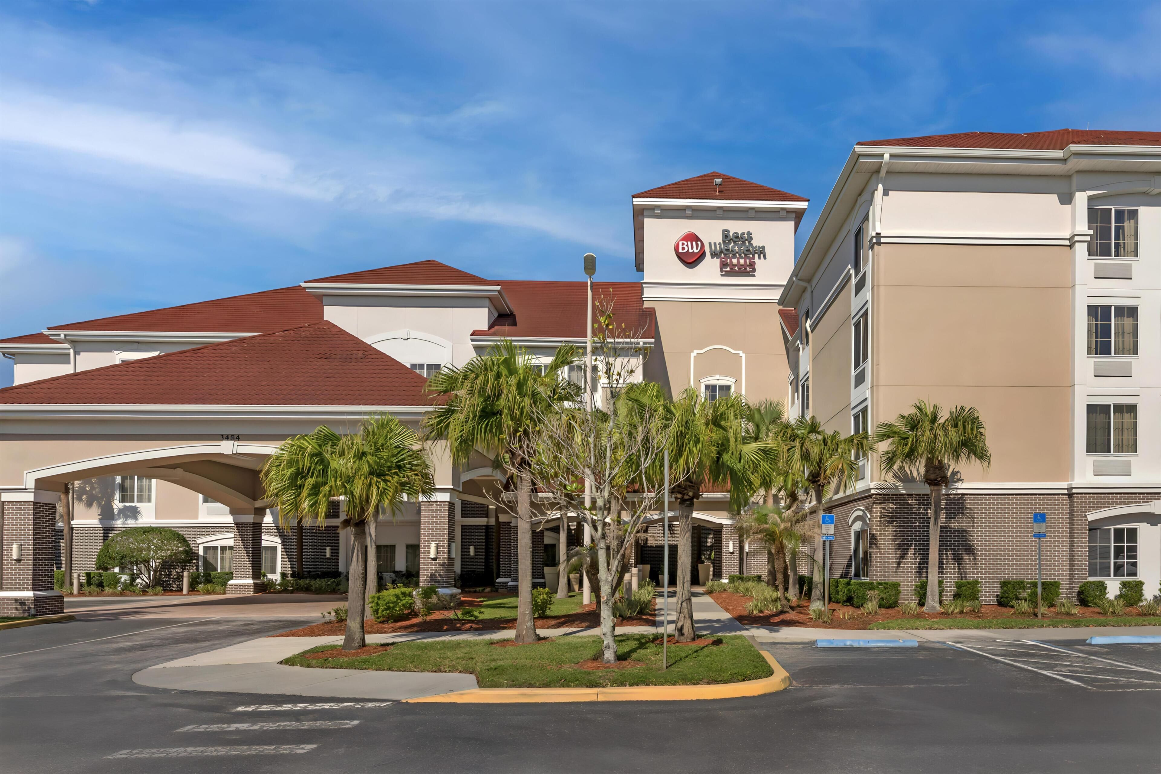 A hotel with a central entrance, palm trees, and a parking lot.