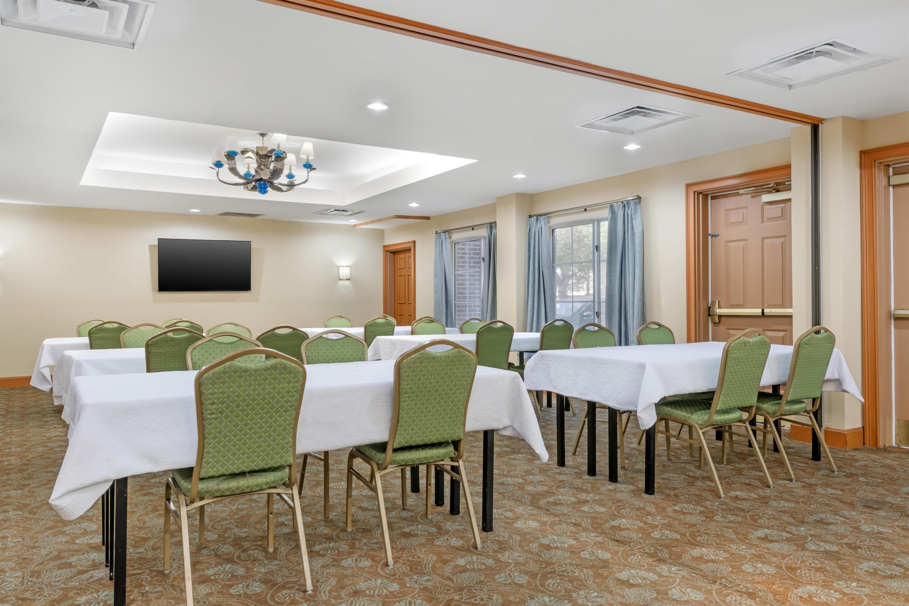 A conference room with tables and chairs, a chandelier, a flat-screen TV, and a patterned carpet.