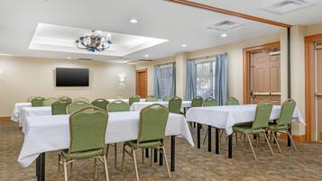 A conference room with tables and chairs, a chandelier, a flat-screen TV, and a patterned carpet.